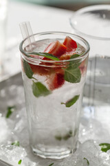 Tasty fresh cold drink with ice, water, mint and strawberry in glass. Closeup.