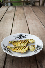 Fried fishes in white flower plate over wooden background. Vertical view.