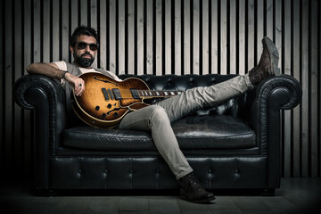 adult caucasian guitarist portrait with electric guitar sitting on vintage sofa. Music singer...