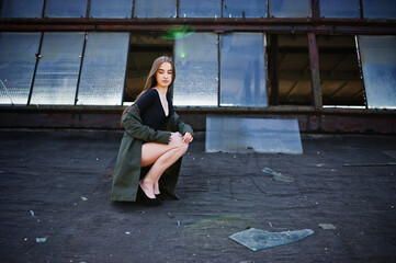 Sexy model girl wit long legs at black lingerie outfit body swimsuit combidress and jacket posed at the roof of abadoned industrial place with windows.