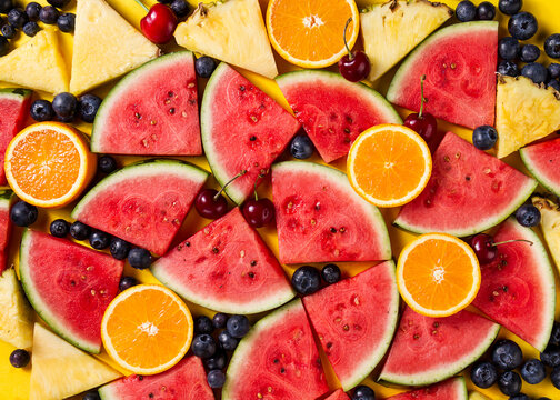 Beautiful pattern with fresh watermelon slices, pineapple, cherries and blackberries on yellow bright background. Top View.