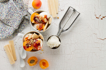 Tasty fresh cold appetizing vanilla ice cream with nuts, apricots, waffles and syrup on white table with ingredients for making dessert. Top View.