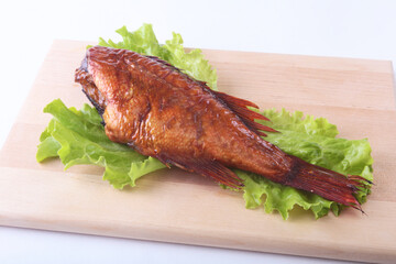 Smoked fish and lemon on green lettuce leaves on Wooden cutting board isolated on white background.