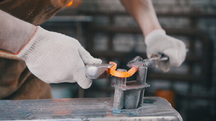 Close up view - hands of Blacksmith with gloves in forge makes steel knife