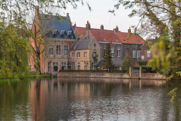 Fototapeta na wymiar The medieval neighborhood at the Begijnhof with brick buildings over lake of Love in Minnewater park in the light of sunset, Bruges (Brugge), Belgium