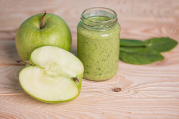 apple with green leaves and smoothie in glass jar on wooden table