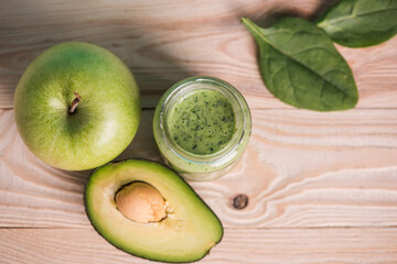 top view of apple with avocado and smoothie in glass jar with green leaves on wooden table