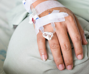 the Asian woman patient hand on IV drip with saline solution, fluid replacement therapy