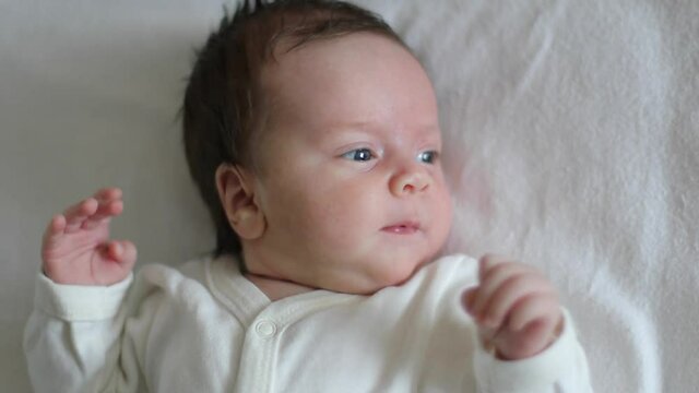 Newborn baby is lies in a cot, looking around and waving his arms (close-up)