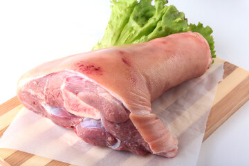 Raw pork knuckle and lettuce leaves on a cutting board. Selective focus. Ready for cooking.