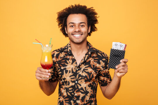Smiling young african man drinking cocktail and holding tickets.