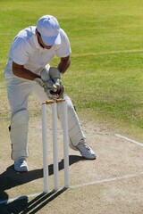 Full length of wicketkeeper catching ball behind stumps on field