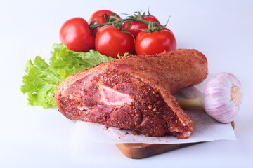 Raw pork knuckle and vegetables, garlic, tomatoes spices and lettuce leaves on a cutting board. Selective focus. Ready for cooking.