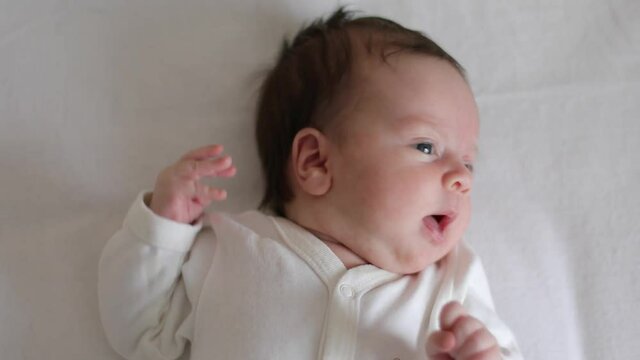 Newborn baby is lies in a cot, looking around and waving his arms (close-up)
