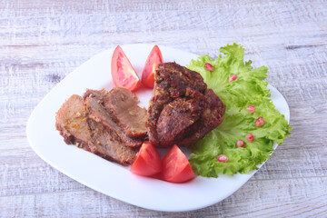 Steak of grilled meat with tomato, lettuce and beans pomegranate on white plate.