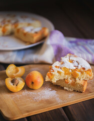 Apricot pie with fresh apricots on a wooden board. Kitchen towel in stripes in the background.