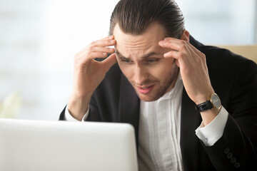 Businessman shocked with fall of company stocks. Stressed entrepreneur with head in hands looking...