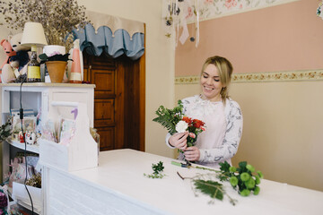 woman florist making bouquet of flowers indoor. Female florist preparing bouquet with roses and carnations in flower shop