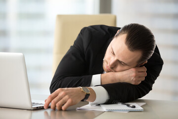 Man lying on work desk with hand placed under head. Businessman fall asleep at workplace after long sleep deprivation. Tired entrepreneur takes break and dozing in office. Chronic fatigue and overwork