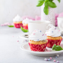 Mini cupcakes with white frosting cream and pink sprinkles on light gray background. Decorated with basil leaves. Party food concept. Copy space.