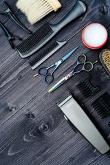 Fototapeta premium Hairdresser tools on wooden background. Top view on wooden table with scissors, comb, hairbrushes and hairclips, free space. Barbershop, manhood concept