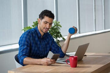 Executive exercising with dumbbells while using mobile phone - Powered by Adobe