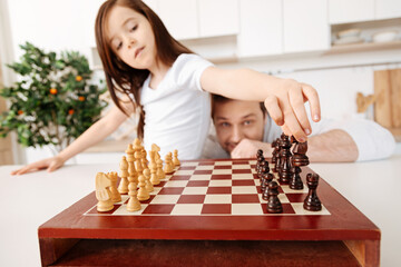 Father watching his daughter moving a knight