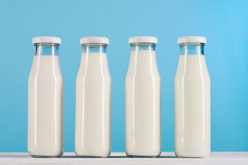 row of glass bottles with milk on tabletop at blue background