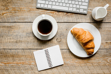 notebook, croissant and cup of coffee on office desk for business breakfast wooden background top view mock-up