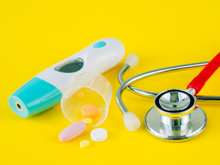 Stethoscope and pills with an electronic thermometer on yellow background, Healthcare and medical concept