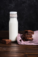 milk in glass bottle and homemade brownie cakes on wooden tabletop