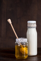 glass bottle of milk with honey in jar on wooden background
