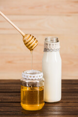 glass bottle of milk with honey in jar on wooden background