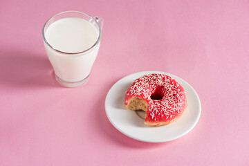 top view of glass cup of milk with donut on plate on pink background