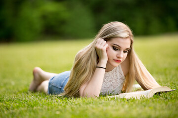 Female blonde teenager in the park with a book.