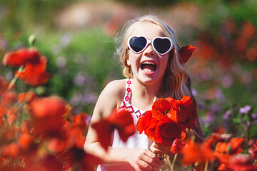 Child girl is wearing sunglasses in spring field with poppies