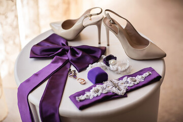 Wedding day. Bridal shoes on high heels, purple accessories for wedding dress, jewelry for bride and wedding ring in ring box on table. Wedding background
