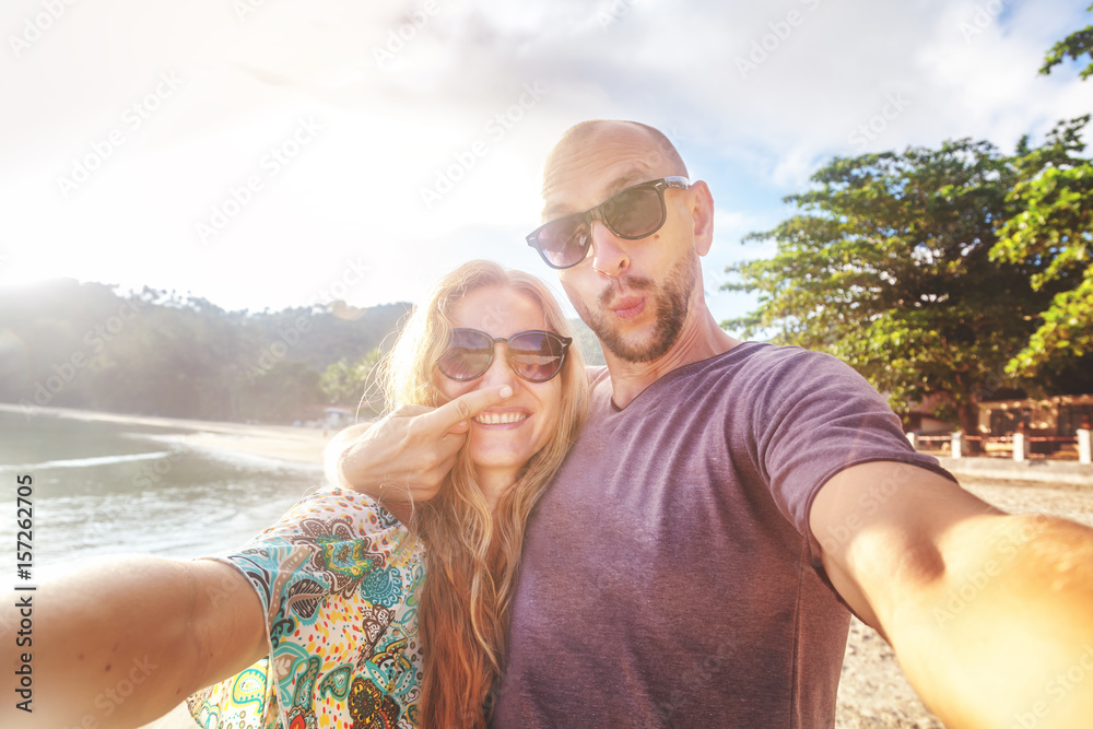 Wall mural Beautiful young funny couple doing selfie on the shore of the tropical sea. Vacation, travel, freedom, happiness and joy.