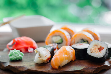 Close up of sushi set. Sushi rolls, nigiri, maki, pickled ginger, wasabi, soy sauce on wooden plate and green tree background. Japanese seafood.