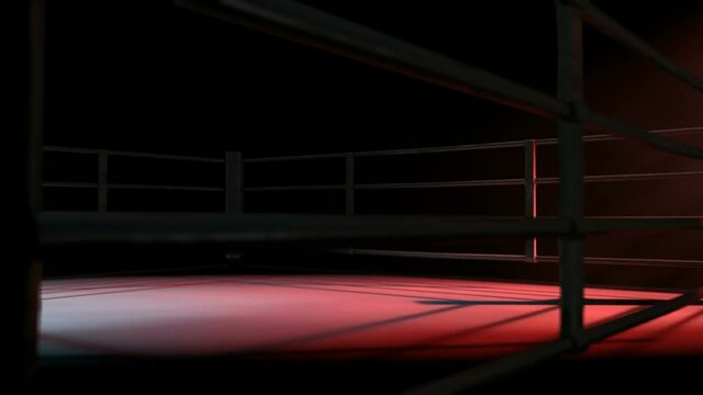 A pan across a empty regular boxing ring surrounded by ropes spotlit in either opposing corner on an isolated dark background
