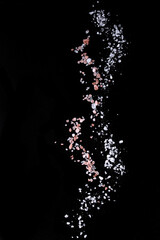 Obraz premium Sifting sea and pink Himalayan salt over black background. Isolated