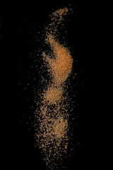Sifting brown cane sugar over black background. Isolated