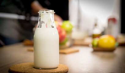 Milk bottle on the wooden table in the kitchen with some other food in the blurry background