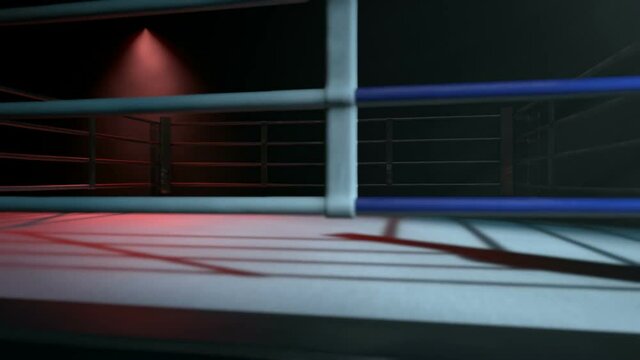 A pan across a empty regular boxing ring surrounded by ropes spotlit in either opposing corner on an isolated dark background