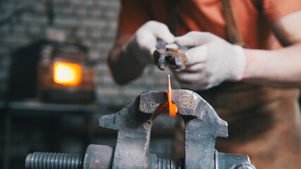 Blacksmith is bending iron rod with hammer - metal workshop, close up