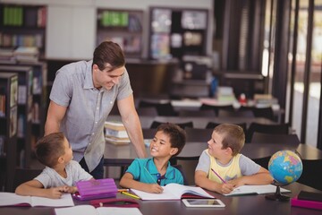 Teacher helping schoolkids with their homework in library