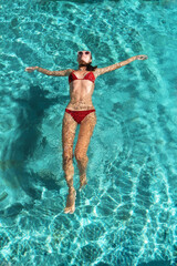 A beautiful young slim sporty woman in a red bikini relaxes on azure water on a tropical island. Travel Concept