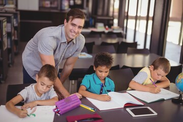 Teacher helping schoolkids with their homework in library