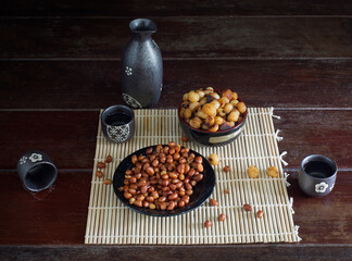 Sake (Japanese alcohol) and snack on bamboo mat all on the wooden table