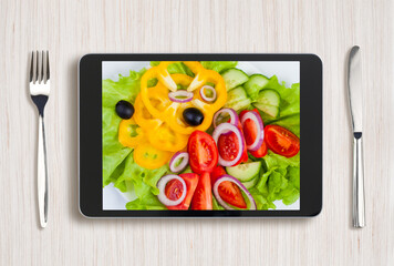 black tablet pc with healthy food on screen and wooden table